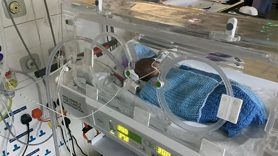 The image shows a baby laying in a MoM incubator.